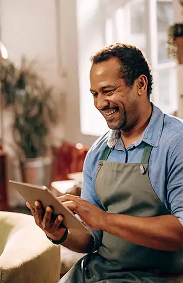 man in an apron sitting down, happily checking his ipad